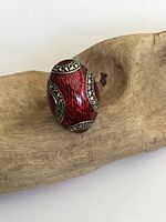 Front angled view of the egg-shaped ring showing red enamel and marcasite details placed on wooden surface.