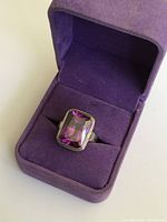 Front view of sterling silver ring with large rectangular purple amethyst glass stone in purple velvet ring box.