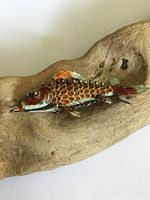 Close-up front view showing enamel colors and articulated details of the fish pendant on natural wood background.
