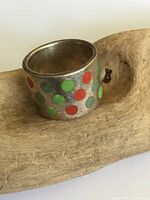 Front view of wide sterling silver ring with red, green, and blue enamel polka dots, sitting on wood surface