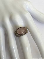 Ring displayed on mannequin hand showing large oval rose quartz set in textured silver band.