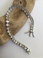 Close-up image showing sterling silver tennis bracelet with clear crystals in a box clasp. Bracelet laid on wooden display surface.