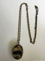 Full view of the necklace showing the metal chain and large oval agate locket with natural banding patterns.