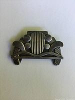 Brooch shaped like a vintage car front, showing detailed design of the grille, headlights and fenders in silver with tarnish.