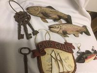 Photo showing two rustic wooden carved fish and a 'Dads Galley' sign with sailing ship, plus antique metal keys on white background
