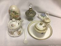 Overview photo showing sugar pot, small spoon, ceramic jar, creamer, decorative egg, and perfume bottle