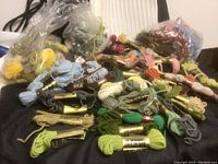 Photo showing various skeins of wool tapestry embroidery floss in multiple colors, some bundled with gold bands, others loose in plastic bags.