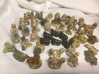 Overview of the entire collection of ceramic tea figurines on white fabric background showing human and animal figures in various colors and shapes.