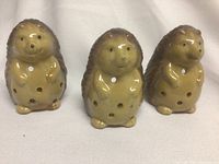 Front-facing photo of three ceramic hedgehog candle holders with belly holes in light brown and tan glaze