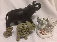 Lot of five elephant figurines including a large black one, green hollow lattice, two white ceramic ones on a floral base, and a small beige figurine.