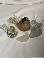 Four glass bird figurines arranged on white fabric background showing different shapes and colors