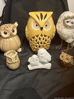 Photo showing six owl-themed items including three ceramic candleholders, two figurines, and one plush owl.