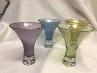 Four colored martini glasses arranged in a row showing front and side angle with clear bases.