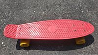 Full view of the 22-inch red plastic Penny Australia skateboard with yellow wheels on pavement.