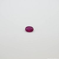 Oval red ruby gemstone measuring approximately 6.1x4.3mm, weighing 0.62 carats shown against a white background.