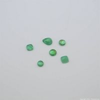 Five small emerald gemstones displayed on a white background showing different cabochon cuts and green color.