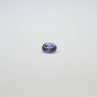Oval cut violet tanzanite gemstone with faceted polish shown on plain white background.