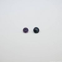 Photo of two round spinel gemstones on white background: one purple, one darker blue-green.