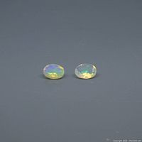 Two oval opal gemstones on a grey background showing their size, shape, and play of color.