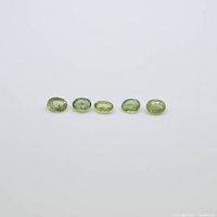 Front view of five oval light green sapphire gemstones arranged in a line on white background