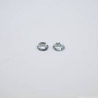 Two oval cut aquamarine gemstones placed side by side on a white background to show clarity and color.