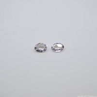 Two oval cut pale pink morganite gemstones placed side by side on a white surface showing color and size