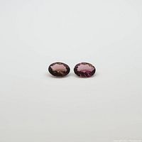 Two oval pink tourmaline gemstones shown from top angle on a white background.