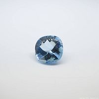 Top view of the cushion-shaped blue topaz gemstone showing facets and transparent blue color.