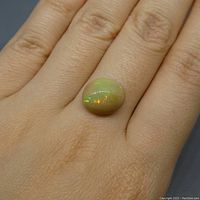Oval cabochon opal gemstone with multicolor play of color placed on finger for scale.
