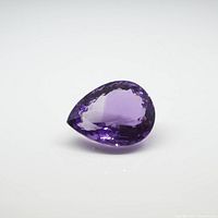 Faceted pear-shaped amethyst gemstone photographed on white background showing purple color and cut.