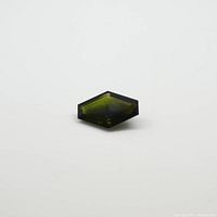 Image showing the coffin-shaped green tourmaline gemstone from one angle, displaying its elongated hexagonal cut and transparency.