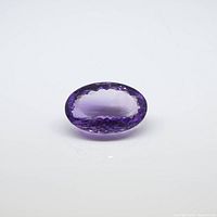 Close-up photo of the oval-shaped amethyst gemstone showing facets and deep purple color on a white background.