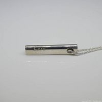 Silver cylindrical pendant on chain, engraved with 'Love'.