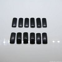 Top down view of twelve rectangular saddle cut black onyx gemstones arranged neatly showing their smooth polished surfaces and black color.