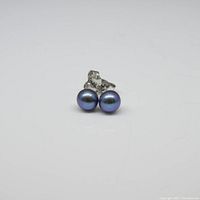 Pair of round bluish black pearls mounted on sterling silver stud posts with butterfly backs shown on white background.