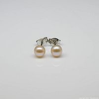 Pair of round pearl stud earrings positioned facing front on a white background to display pearls and silver posts.