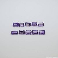 Top-down view of 10 baguette cut purple amethyst gemstones arranged in two rows on a white background, showing size and color consistency.