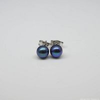 Front view of the pair of round bluish black pearl stud earrings set in .925 sterling silver on a white background.