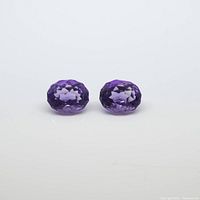 Front view of two purple faceted amethyst gemstones on white background