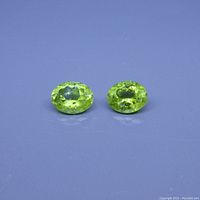Two oval faceted green peridot gemstones on a blue background, showing transparency and brilliance.