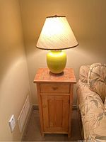 Tall antique pine end table with ceramic table lamp on top, placed next to a floral patterned sofa in corner of room.