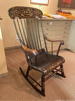 Antique wooden rocking chair with floral painted crest rail, spindled back, curved armrests, and carved rockers.