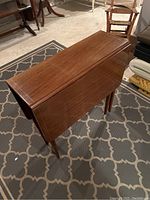 Photo showing the table with one drop leaf extended, highlighting the wood grain and tapered legs.