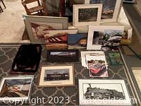 Wide shot showing collection of framed and unframed train-themed art laid on floor, variety of sizes and styles visible.