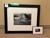 Two framed black and white photographs shown side by side on floor near wall, largest frame is black with wide white mat, smaller frame is black with white mat