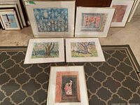 Wide photo showing all five framed artworks arranged leaning against wall and on floor; various colors, styles, and sizes visible.