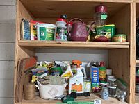 Shelves filled with assorted gardening supplies including bird feeder, red watering can, seed packets, gardening gloves, and multiple bottles of fertilizers and garden chemicals.