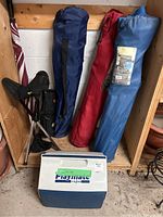 Photo of three fabric covered folding camping chairs, a small tripod folding stool, a large cooler labeled Playmate by Igloo, and the edge of a large golf umbrella with red and white panels.
