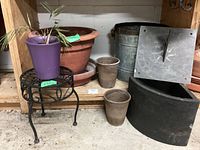 Wide view of all items showing various planters, metal bucket planter, black semicircular planter, purple plastic planter with small palm plant, and sundial.
