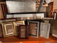 Multiple picture frames stacked on shelf showing variety of frame styles and sizes